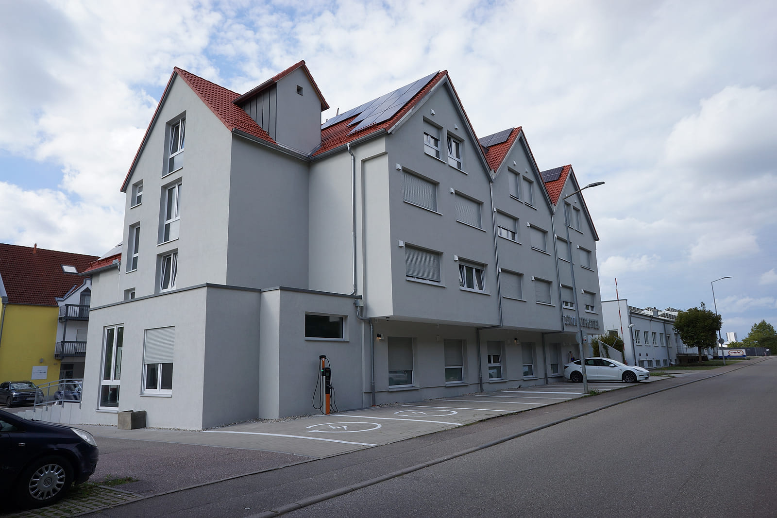 Das SMARTHOTEL Aalen von außen: weiß verputztes Gebäude mit drei Giebeln, rotem Dach und Photovoltaikmodulen.
