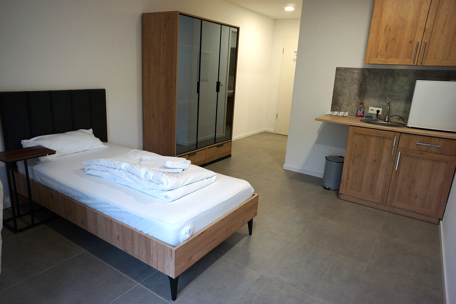 Budget Einzelzimmer mit Küche: Einzelbett, Spiegelschrank und eigene Küchenzeile im selben Raum.