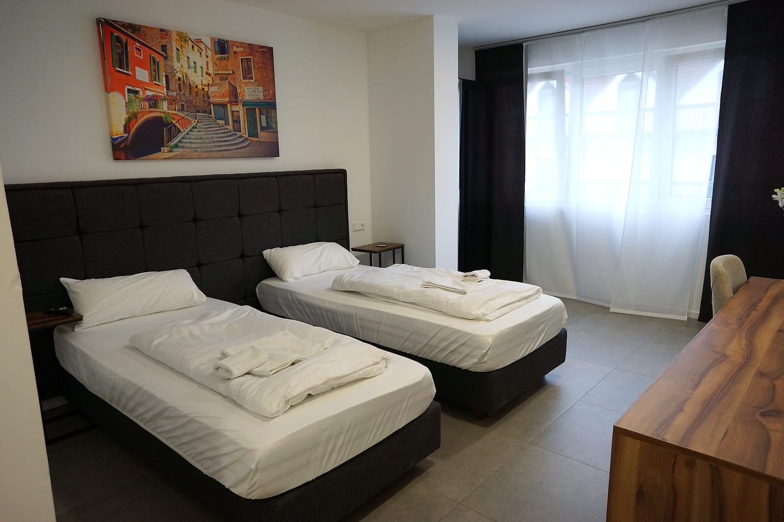 Deluxe Doppel- / Zweibettzimmer mit zwei Betten vor dunklem gepolstertem Kopfteil und Fenster.
